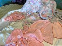 Overview of nine pastel-colored hand knit baby clothing items including sweaters, hats, and booties arranged on a surface.