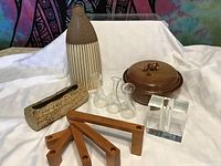 All lot items displayed on white cloth under bright lighting showing arrangement of pottery, glass vases, candle holder, wooden stands, and log planter.
