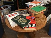 Photo showing carved round wooden folding table top with assorted books placed on top.