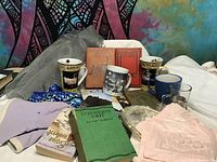 Full view of mugs, books, napkins, glasses on surface against colorful tapestry
