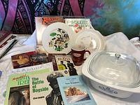 Photo showing a large Corning Ware casserole dish, Tim Hortons mug, several books, and decorative plates arranged together.