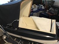 Side view of pram with canopy partially open, showing black exterior and cream interior.