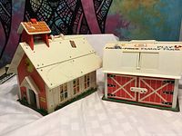 Vintage Fisher-Price schoolhouse and farm barn playsets side by side on a tableshowing exterior details
