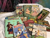 Photo showing vintage girl's books including Heidi series, Brownies Annual, Donna Parker, Wendy, Nancy Drew and others arranged on white fabric
