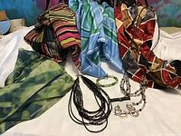 Array of five colorful scarves with various patterns and colors including striped, tie-dye, and geometric prints spread out on a surface with jewelry items.