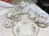 Full set arranged on cloth, showing teapot, cups, saucers, sugar bowl, creamer, plates and butter pat.