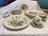 Overview of the entire set showing large platter, stacked plates, bowls, cups, saucers, and cream pitcher decorated with multicolored floral patterns.