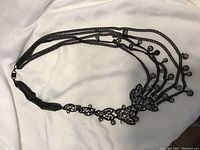 Full view of the necklace showing the overall unique design with multiple chain strands and decorative leaf shapes and round charms.