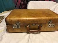 Closed view of vintage brown leather suitcase showing metal clasps and handle.