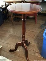 Round wooden occasional table with polished top, turned central pedestal, and three curved legs with casters.