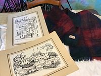 Two matted prints by Julio Amaro showing Portuguese scenes and a folded plaid wool and mohair shawl with pockets and fringed edges.