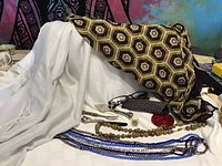 Display of two fabric wraps, beaded jewelry strands, reading glasses with case, metal thimble, and three-piece silver-toned cheese set on a white surface.
