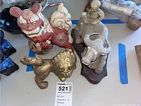 Photo showing all three figurines together: ceramic red/white lion, gray ceramic elephant with child, and brass lion.