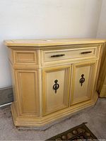 Front-side angle of yellow vintage buffet cabinet showing drawer and double doors with metal pulls.