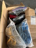 Box containing multiple sealed plastic bags of coiled cables in various colors: yellow, gray, blue, and black, also a Nikon camera base box visible inside.