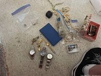 Various costume jewelry and watches arranged on a floor surface, including wristwatches, bracelets, faux pearl necklaces, and brooches.
