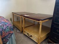 Two wood end tables placed side by side beside a bed and a dresser, showing overall construction and condition including surface wear and scratches.