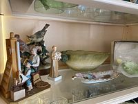 Shelf with Norman Rockwell figurine, angel figurine, decorative birds, a large green bowl and floral dish.