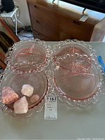 Photo showing four pink glass plates with distinctive reticulated edge and sunburst pattern, arranged in a cluster on a surface.