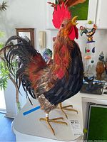 Full view of the decorative feathered rooster figurine standing upright, showing colorful feather details and wire legs.