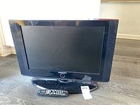 Full image of Samsung 22-inch TV with remote control placed in front, both on a dark wood surface.