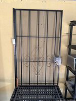 Rear or opposite side view of black metal screen door showing lock handle and vertical bars.