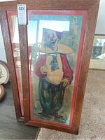 Framed clown print with trumpet and red jacket showing full figure in a wooden frame with reddish mat.