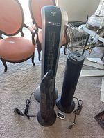 Three black tower fans positioned on carpet; remote control visible beside the tallest fan.