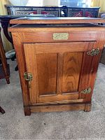 Front view of closed vintage wooden wine cabinet showing stained finish, metal latch and hinges, and rectangular metal label plate.