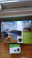 Boxed Deluxe Double Flocked Airbed with mountain camping scene on packaging and 6V battery pump box beneath it.