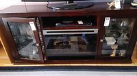 Front view of dark wood TV cabinet with electric fireplace center and glass door storage on each side containing glassware.
