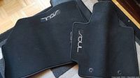 Photo showing black carpet car mats for Kia Soul with 'Soul' embroidered and securing holes visible.