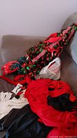 Foil Christmas tree decorated in red and green tinsel with pink ribbon, laying on a couch along with costume garments.