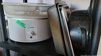 West Bend Crockpot on shelf with multiple metal trays and a black speckled roaster
