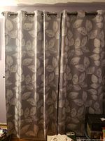 Two gray curtain panels with a white leaf pattern hung by metal grommets on a curtain rod.