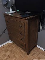 Side angle view of vintage wooden dresser showing four drawers, metal pulls, and wood grain finish. Shows wear consistent with age.