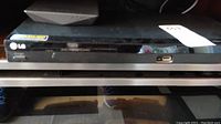 Front view of the LG DVD player showing the glossy black panel, USB port, disc tray, and brand logo.