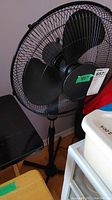 Photo showing the black 40-inch floor fan with three large blades and black protective wire cage, standing next to various household items