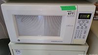 Front view of white GE microwave oven showing door with mesh window and digital control panel on the right side.