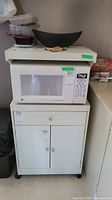 Front view of the white microwave stand with a drawer above cabinet doors, microwave on top is not included