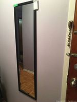 Full length rectangular mirror with black frame mounted on wall near door, showing full vertical view.