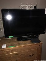 Front view of Philips 27-inch flat screen TV on black stand showing TV brand and remote taped at back.