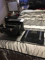 Black fold-out make-up box displayed on patterned bedspread, showing compartments and storage feature