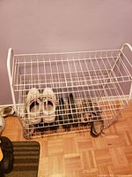 Photo of white metal shoe rack with three wire grid shelves, holding various shoes for scale only.