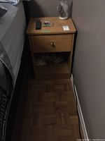 Front view of wooden side table showing drawer with round wooden knob and open shelf beneath.
