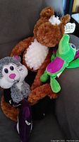 Four stuffed animals grouped together on couch: brown bear, green frog, gray wolf, and black bat.