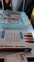 Travel water bottle box and base of flatware box together, clear view of bottle packaging and other boxed item