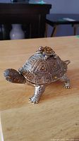 Photo showing brass turtle trinket box with amber-colored stones and small turtle on lid