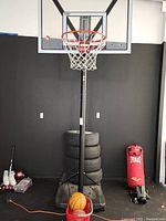 Full view of the basketball hoop with post, basket balls, base with no tires, and surrounding items