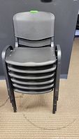 Stacked set of 6 black plastic chairs showing the front view and armrests.